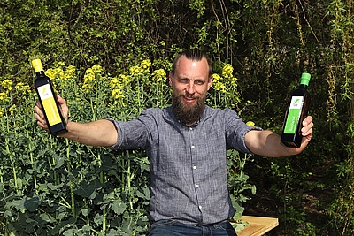 Thomas Raab von der Öl Mühle Raab hält zwei Biospeiseölflaschen in der Hand
